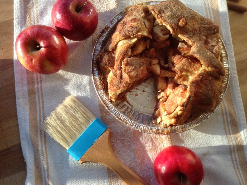 Apple pie with one slice cut out and apples around it