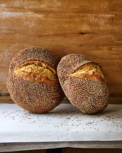 Two loaves of Sesame Semolina leaning against a wooden wall