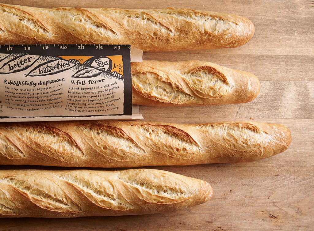 Four French baguettes, one in a paper bag