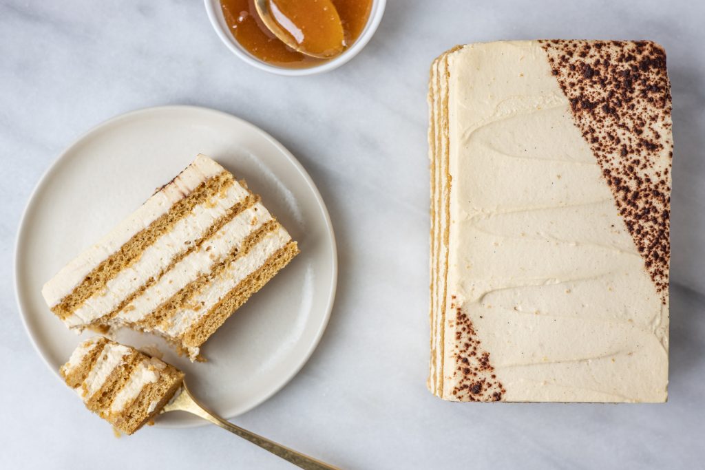 A full Mézes Krémes torta with one slice of cake on a white plate 