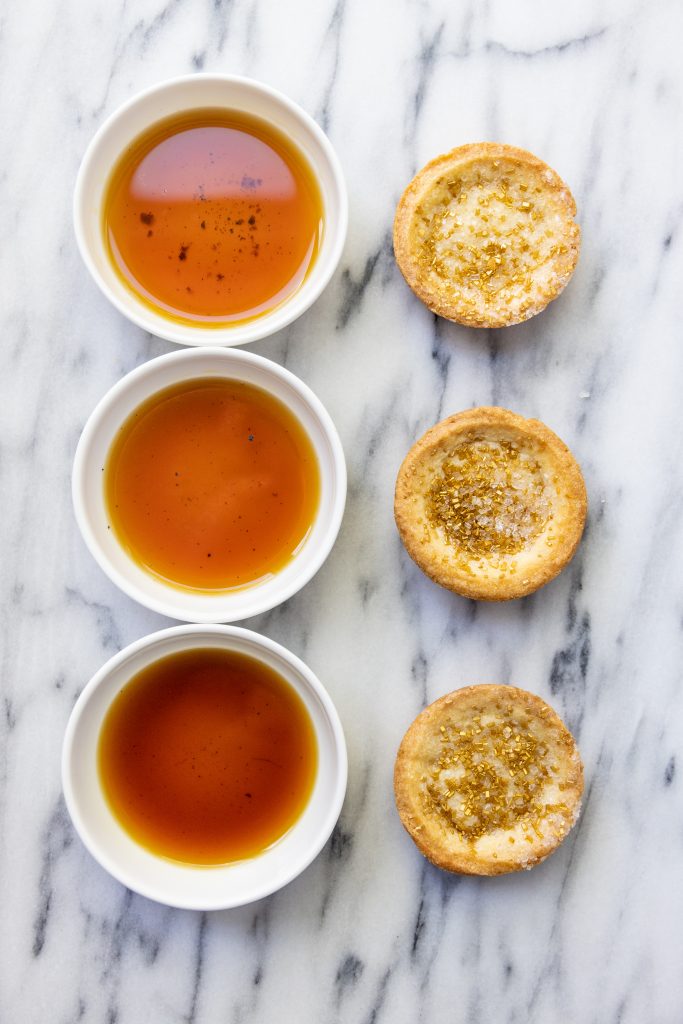 three small white dishes filled with vanilla extracts, each with a cookie beside it