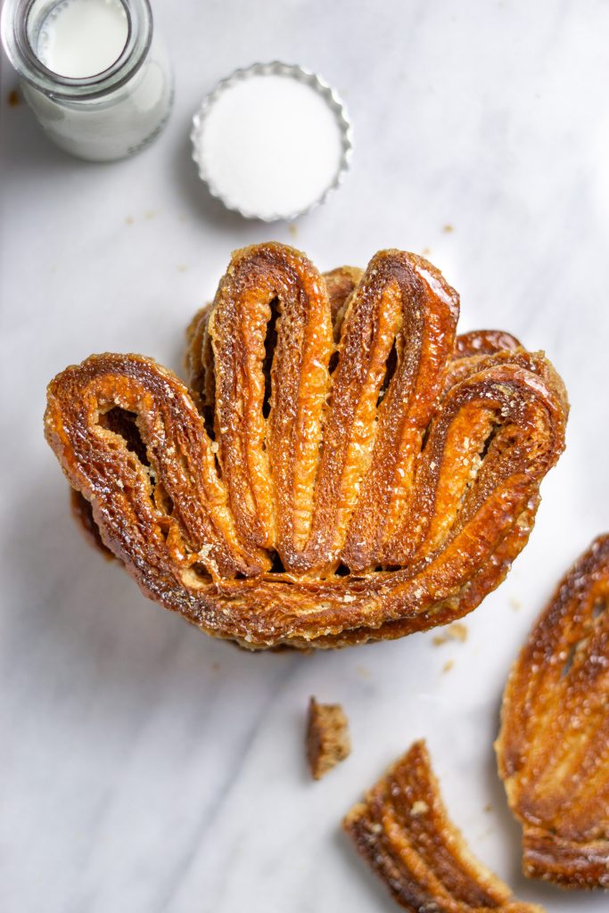 an overhead view of a stack of palmiers on a white marble surface with a glass jar of milk