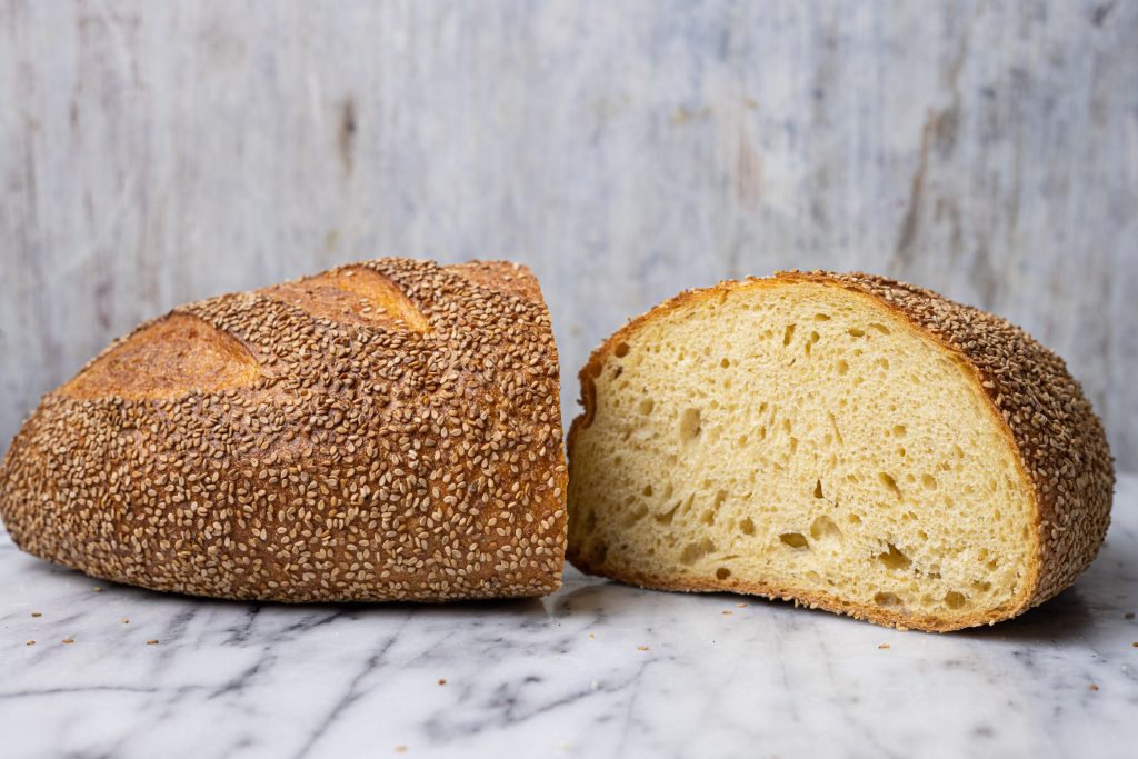 a loaf of Sicilian Sesame Semolina bread, cut in half, with one half tilted towards the viewer