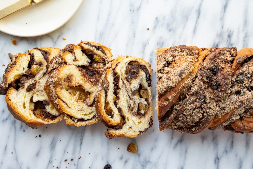 overhead view of a chocolate raisin babka on a marble surface with 3 slices cut