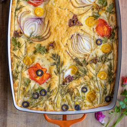 A pan of garden focaccia decorated with onions, bell peppers, and herbs to look like a garden scene.