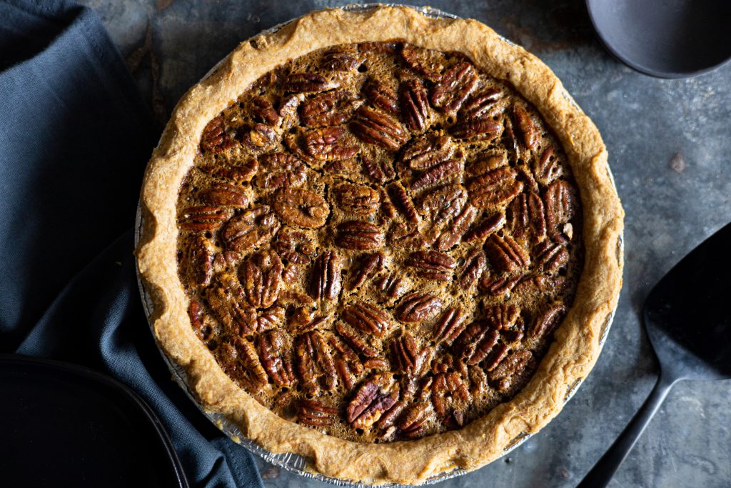 overhead view of a whole pecan pie on a dark grey surface with a pie server