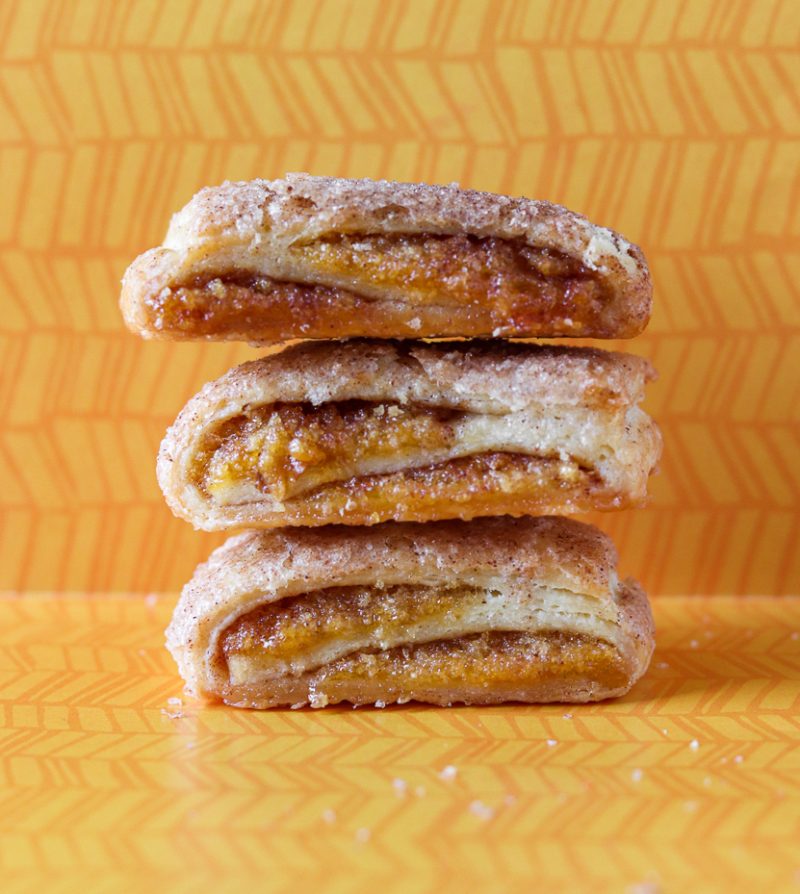 A stack of 3 apricot rugelach sit on an orange patterned background