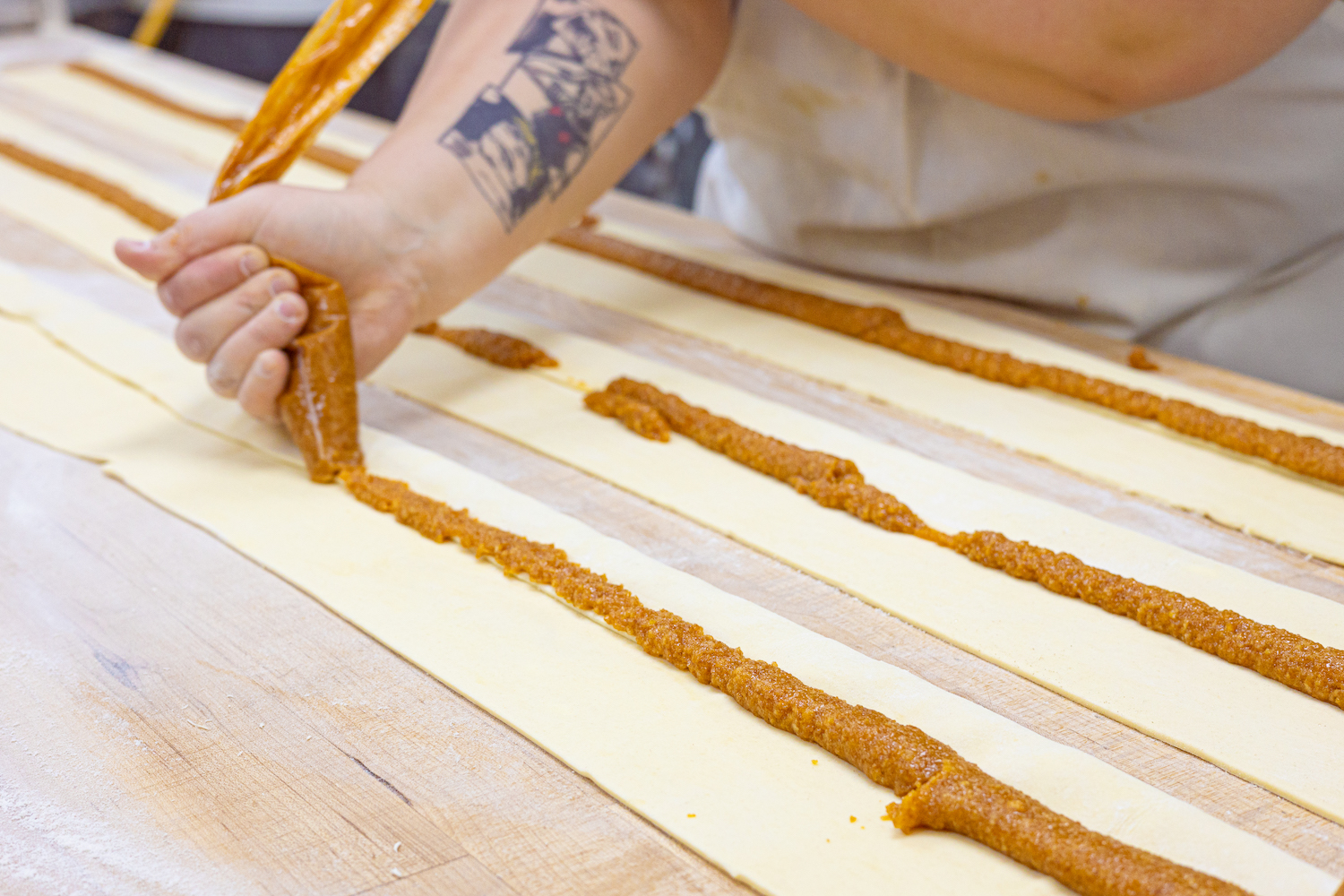A hand is seen piping apricot rugelach filling onto long, flat sheets of dough.