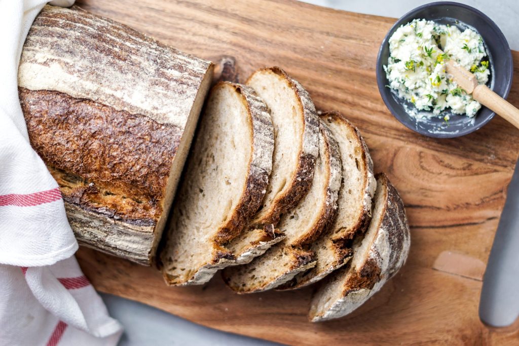 overhead view of a loaf of true north on a wooden cutting board with a few slices cut and some compound butter