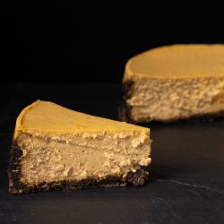 a pumpkin cheesecake on a black surface with one slice in front