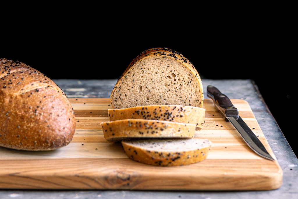 two loaves of Chernushka Rye bread on a wooden cutting board, one with cut slices tipping forward
