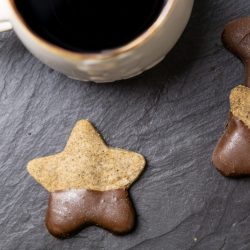 Chocolate-dipped espresso star cookies on a black slate surface with a cup of coffee just visible at the top of the frame