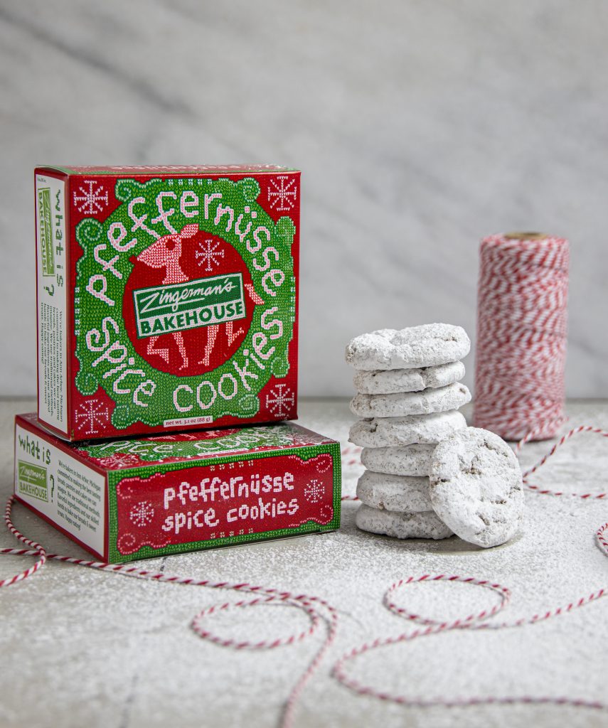 Two red and green boxes of Pfeffernüsse cookies with a stack of cookies next to them and a spool of red and white twine