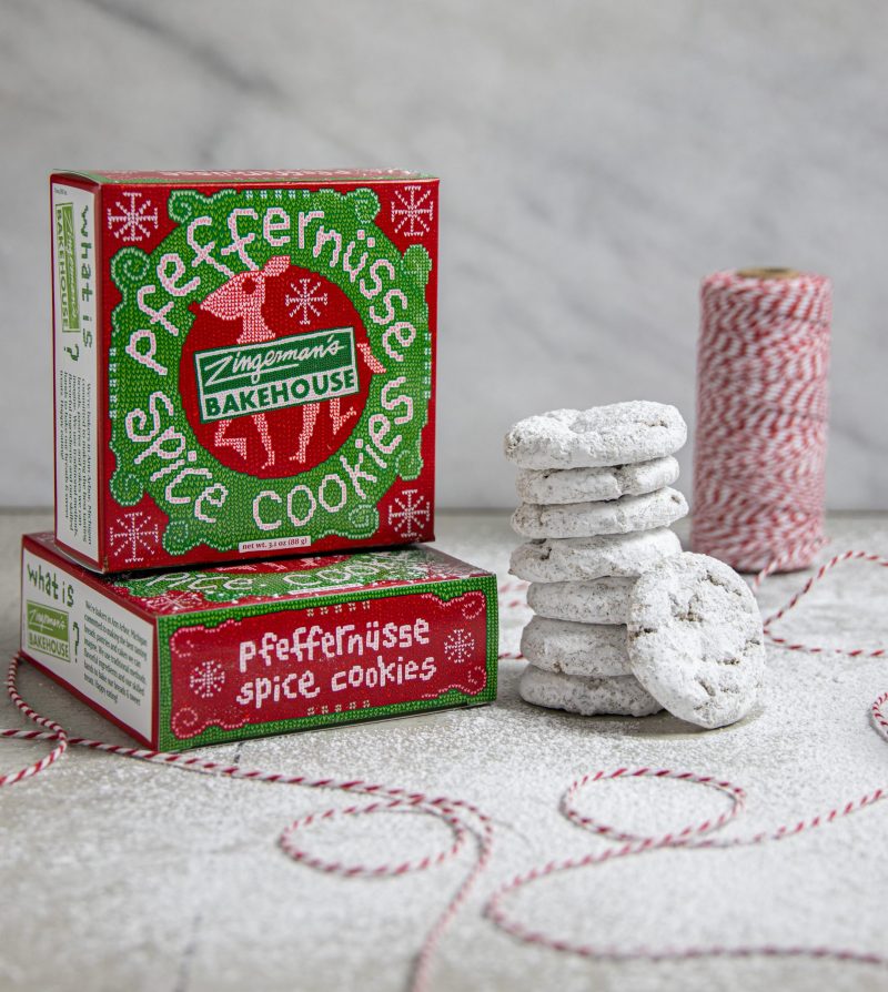 red and green boxes of pfeffernüsse cookies with a stack of cookies next to them and a spool of red and white twine