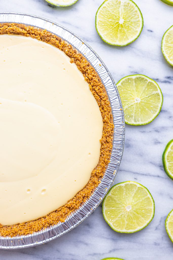 Overhead partial view of a whole Key Lime Pie on a marble surface with slices of limes