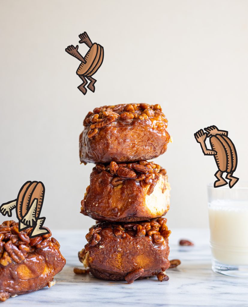 one Obama Bun next to a stack of three Obama Buns and a glass of milk with illustrated anthropomorphic pecans jumping on them