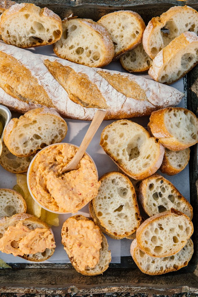 A Rustic Italian Baguette alongside a slices of one and a container of bacon pimento cheese