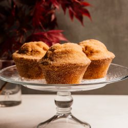 Sugar Crisp Muffins on a glass cake stand in front of red fall foliage.