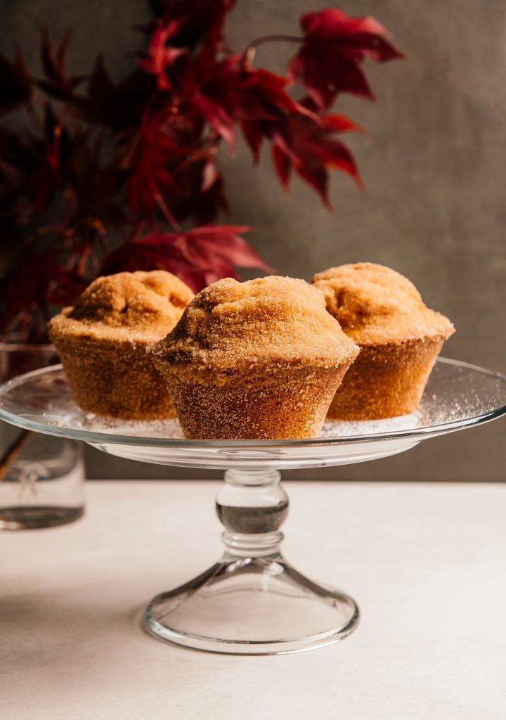 Sugar Crisp Muffins on a glass cake stand in front of red fall foliage.