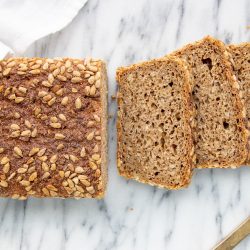 Ari's Pick: Dinkelbrot dinkelbrot, partially sliced on a marble surface with a white tea towel partially covering the end and a gold knife next to it