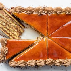 an overhead view of a dobos torta cake with one slice pulled out and laid on its side to reveal the layers