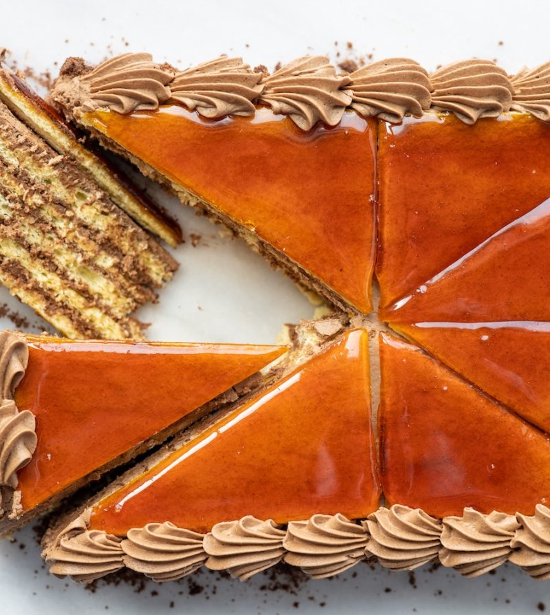 an overhead view of a dobos torta cake with one slice pulled out and laid on its side to reveal the layers