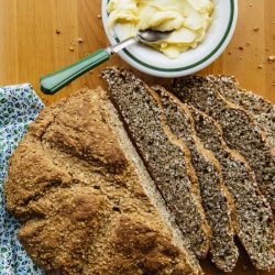 Irish Brown Soda Bread partially sliced with a dish of butter next to it.