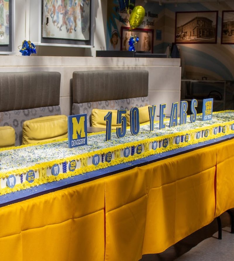 a long cake decorated in maize and blue colors on a yellow tablecloth-covered table