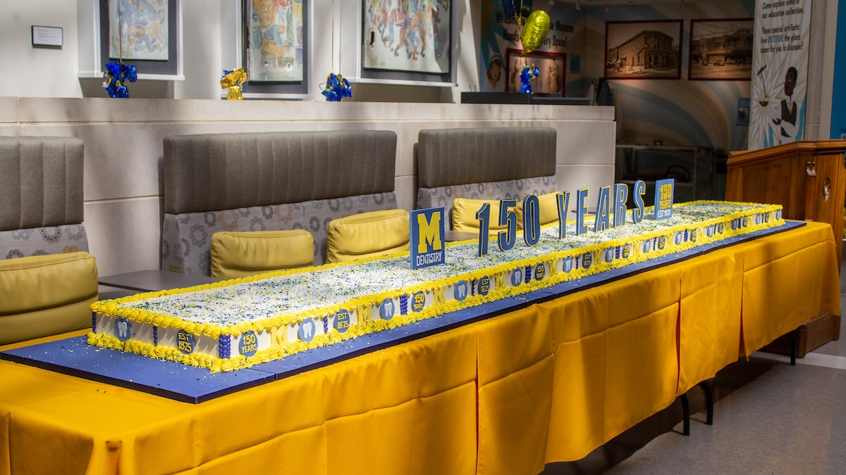a long cake decorated in maize and blue colors on a yellow tablecloth-covered table