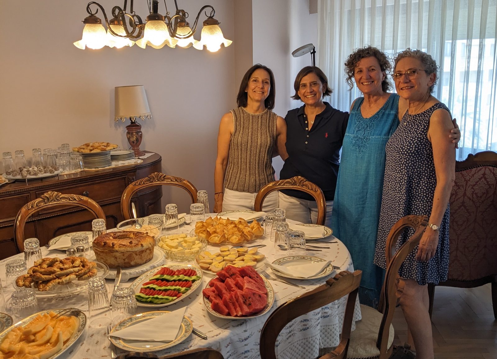 4 women standing next to a table filled with food
