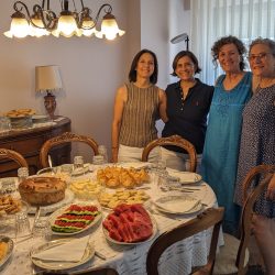 4 women standing next to a table filled with food