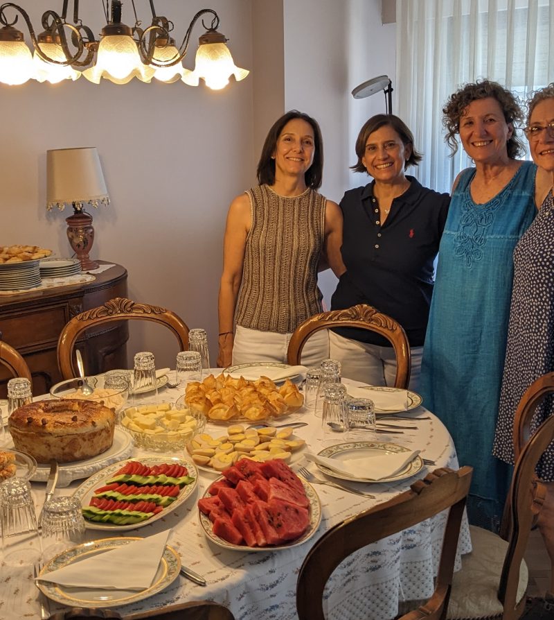 4 women standing next to a table filled with food